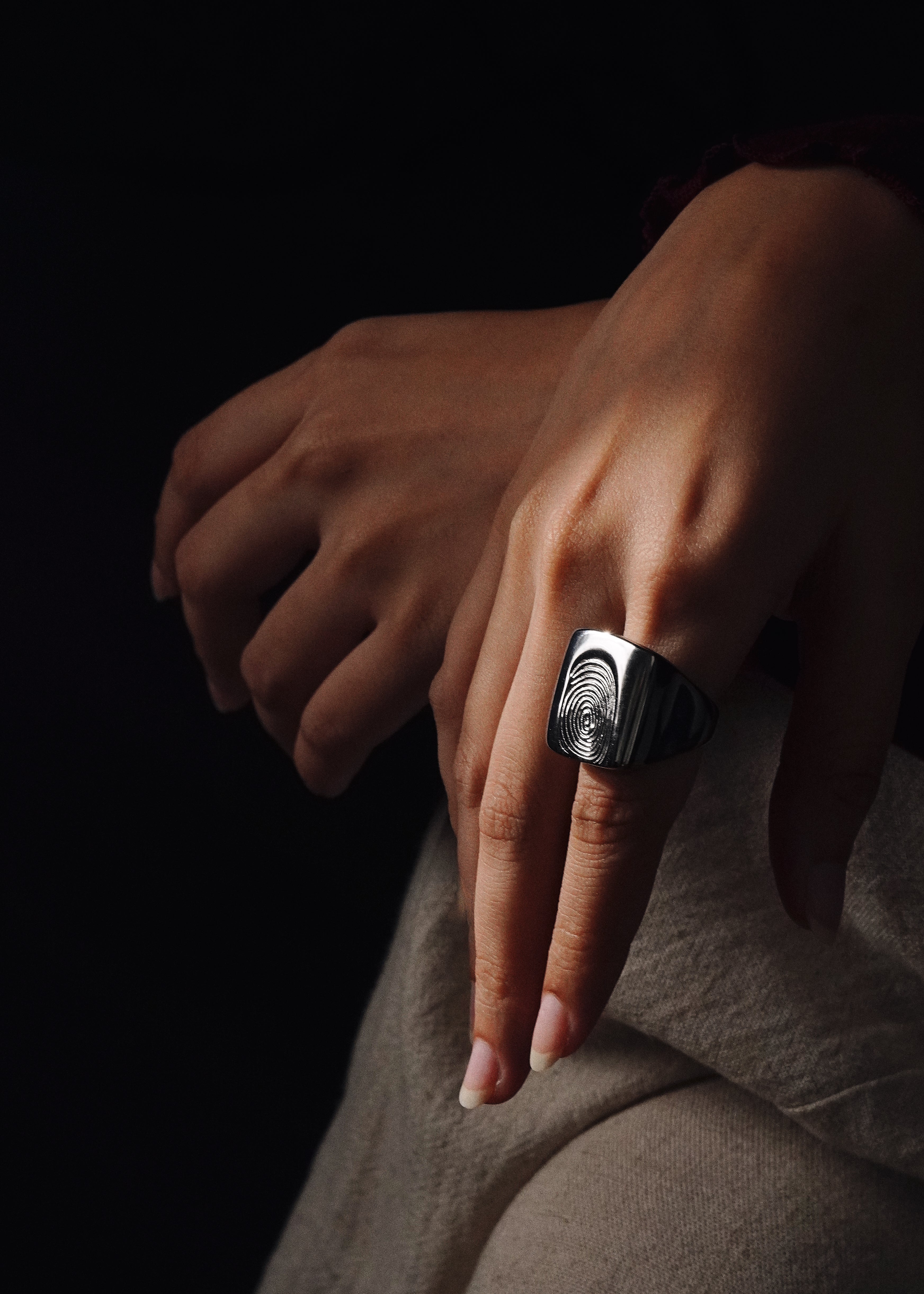 Hand wearing a silver ring with a dark background