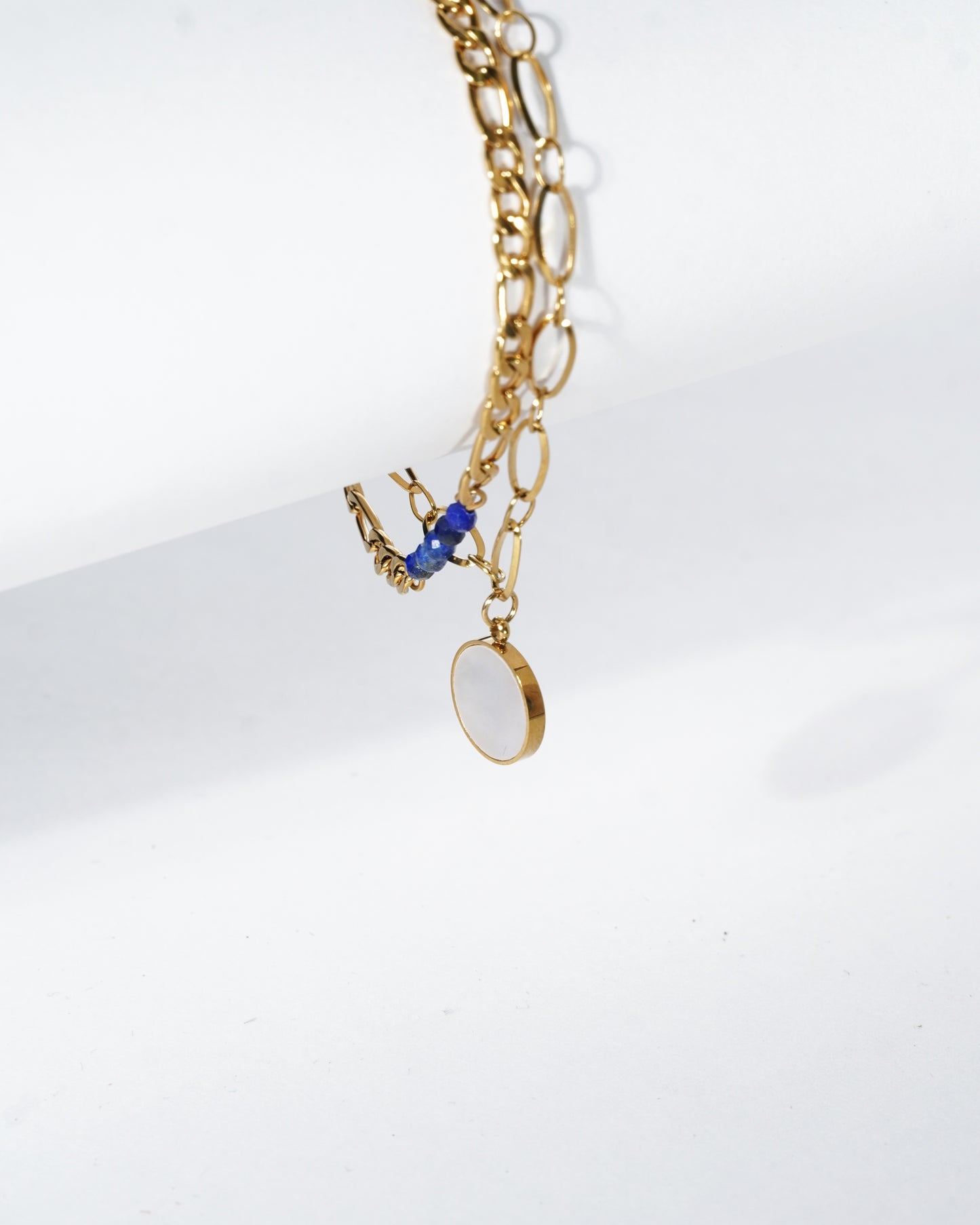 Gold chain necklace with blue pendant on a white background
