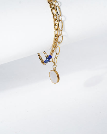 Gold chain necklace with blue pendant on a white background