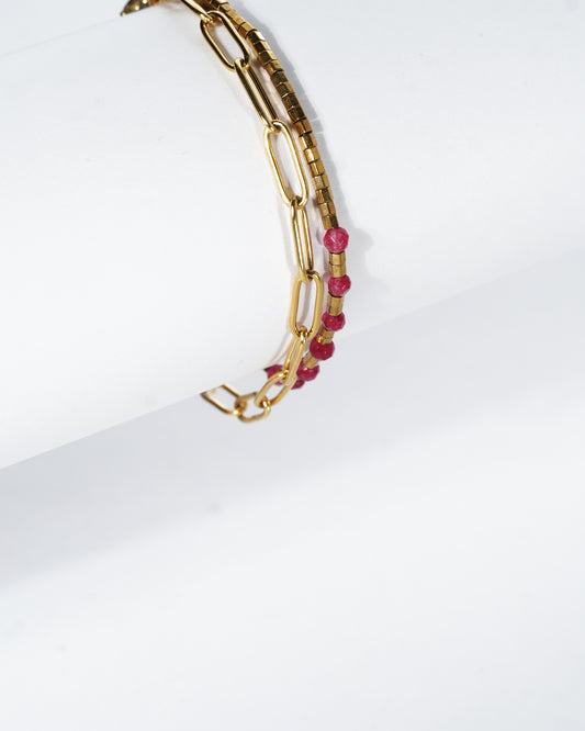 Gold chain bracelet with pink beads on a white background